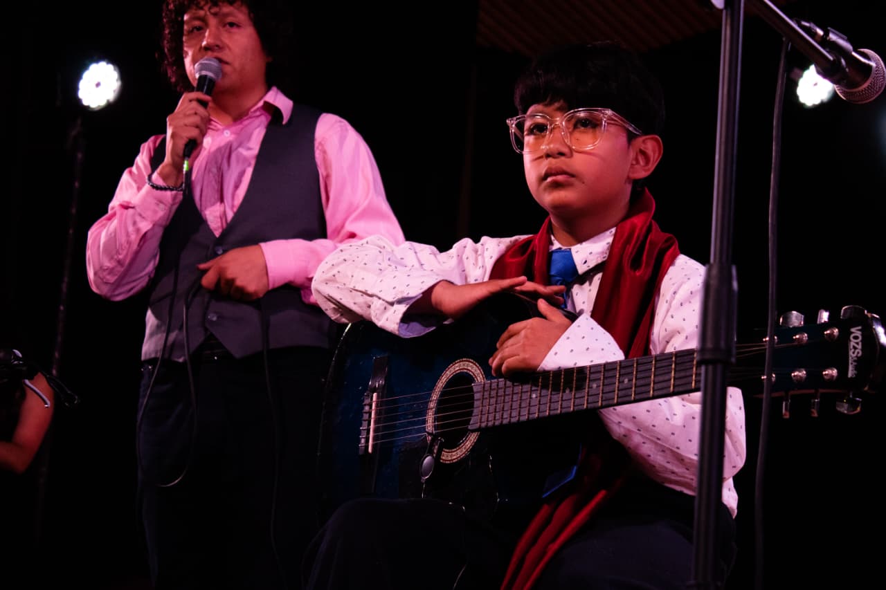 Docente acompañando a un estudiante de guitarra sobre el escenario